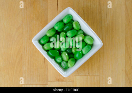 Une pile de green jelly beans dans un bol blanc contre un fond bloc de boucher Banque D'Images