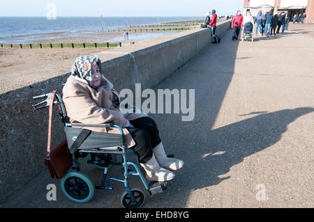 Une vieille dame en fauteuil roulant tient chaud l'hiver soleil sur la promenade de Hunstanton. Parution du modèle. Banque D'Images