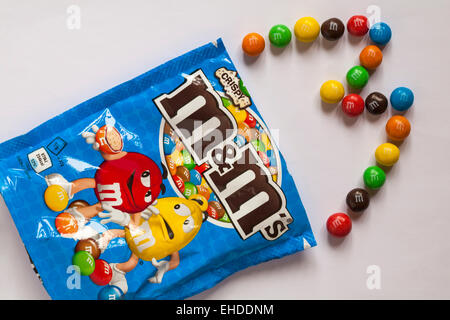 Ouvert sachet de M&Ms croustillant avec contenu répandu afin d'épeler lettre M isolé sur fond blanc Banque D'Images