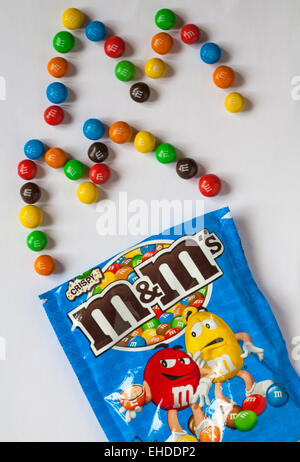 Ouvert sachet de M&Ms croustillant avec contenu répandu afin d'épeler les lettres M isolé sur fond blanc Banque D'Images