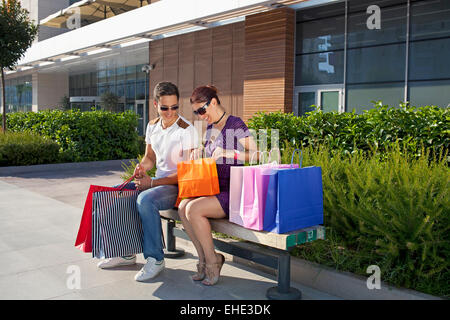 Couple assis sur un banc en face d'un centre commercial avec des sacs de shopping, de détente Banque D'Images