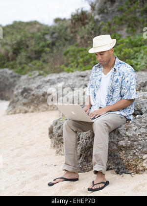 L'homme à l'aide d'Apple Macbook Air ordinateur portable ordinateur portable pour travailler sur la plage pendant les vacances Banque D'Images