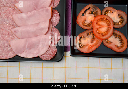 Salami divers et les tomates sur des assiettes en céramique noire Banque D'Images