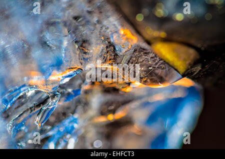 Goutte d'eau de la fonte des glaces à la gouttière, avec des reflets de ciel bleu et jaune les rayons du soleil passant à travers. Banque D'Images