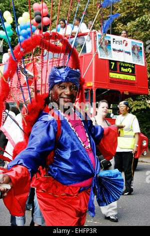 Mas danseur à Notting Hill Carnival avec London bus derrière. Banque D'Images