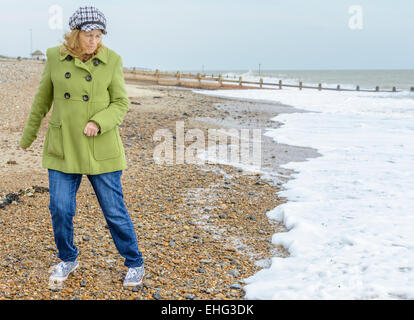 Femme d'âge moyen en esquivant les vagues sur une plage au bord de la mer. Banque D'Images