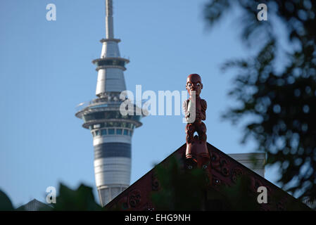 Une sculpture d'un guerrier Maori monte la garde sur un marae tandis que la Sky Tower moderne domine la ville de Auckland en Nouvelle Zélande Banque D'Images