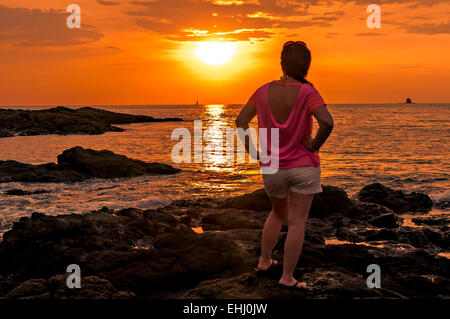 Femme debout sur les rochers en regardant le coucher du soleil Banque D'Images