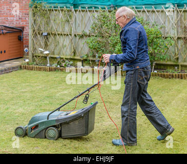 Vieil homme de tondre la pelouse dans un jardin. Banque D'Images