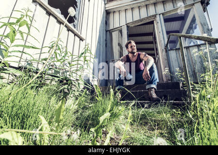Un jeune homme assis à l'extérieur de maison abandonnée et la fumée de cigarettes. Banque D'Images
