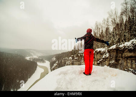 Caucasian hiker standing with arms outstretched on snowy hilltop Banque D'Images