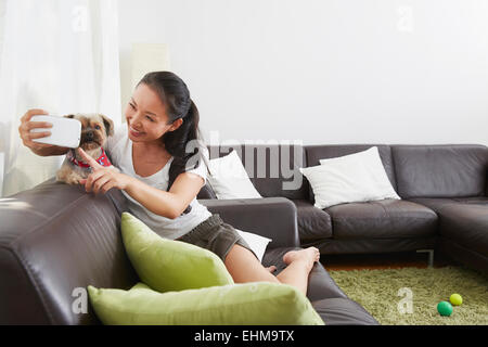 Femme chinoise en tenant selfies téléphone cellulaire avec dog in living room Banque D'Images