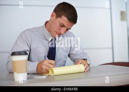 Caucasian businessman writing on notepad in office Banque D'Images