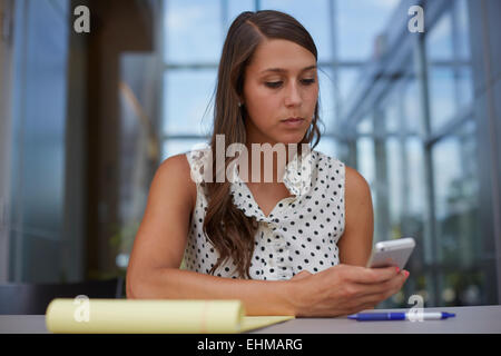 Mixed Race businesswoman using cell phone at desk Banque D'Images
