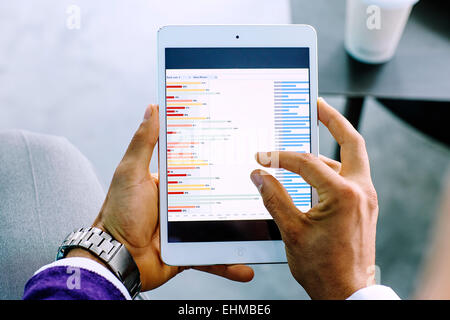 Mixed Race businessman examining graph on digital tablet Banque D'Images