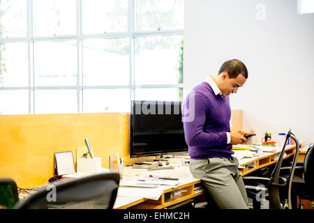 Mixed Race businessman using cell phone at office desk Banque D'Images