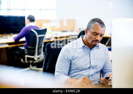 Businessman using cell phone at office desk Banque D'Images