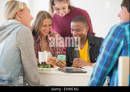 Les adolescents using cell phone at table Banque D'Images