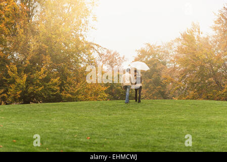 Couple walking with umbrella in park Banque D'Images