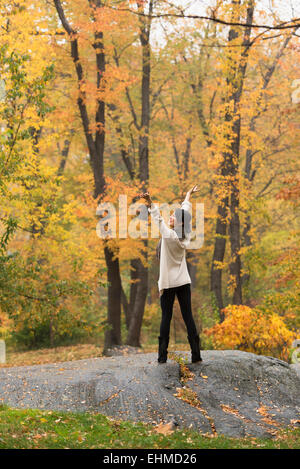 Asian woman cheering with arms outstretched on rock in park Banque D'Images