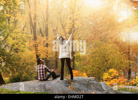 Woman cheering with arms outstretched près de petit ami en park Banque D'Images