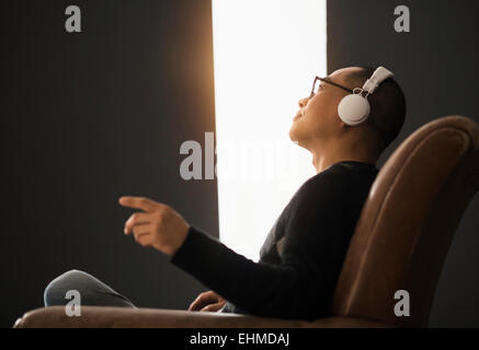 Korean man listening to headphones in armchair Banque D'Images