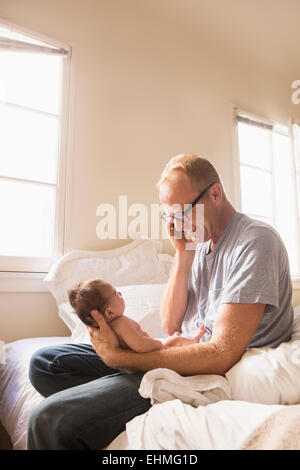 Père talking on cell phone et holding baby on bed Banque D'Images