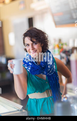 Mixed Race woman holding cup of coffee in cafe Banque D'Images