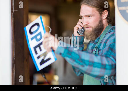 Serveur Caucasienne sur téléphone hanging open sign sur fenêtre cafe Banque D'Images