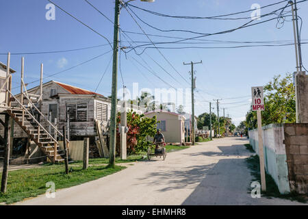 Retour rue de Caye Caulker montrant les maisons typiques et l'homme sur tricycle Banque D'Images