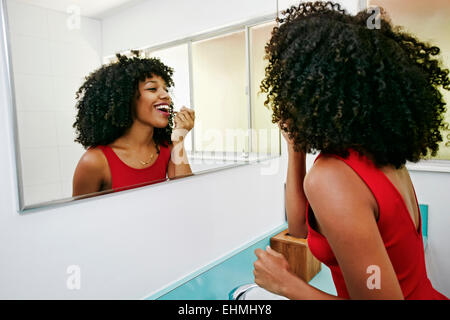 Mixed Race woman applying makeup in mirror Banque D'Images