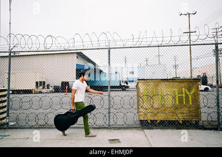 Mixed Race musicien réalisation guitar case on sidewalk Banque D'Images