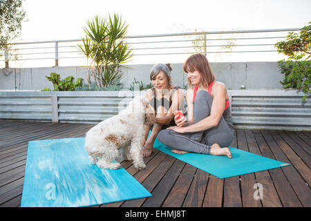 Les femmes avec chien using cell phone on exercise mat Banque D'Images