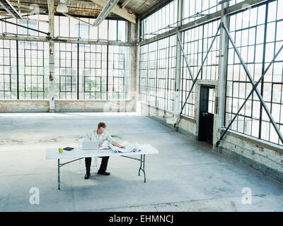 Caucasian businessman reading blueprints in empty warehouse Banque D'Images