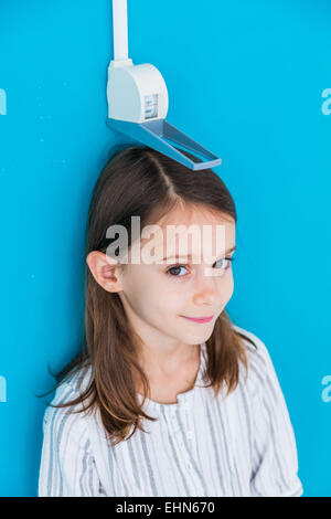 7-year-old girl measuring elle-même contre une jauge de hauteur. Banque D'Images