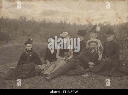 Ce portrait de famille du début du XXe siècle capture un groupe d'individus posés à l'extérieur, typique de la photographie du début du XXe siècle. L'image reflète la mode et la dynamique familiale de l'époque, avec des individus vêtus de vêtements d'époque. Banque D'Images