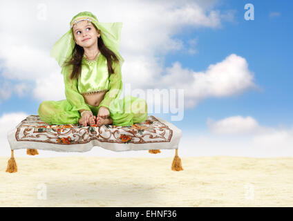 Peu arabian girl sitting on tapis volant avec le fond de ciel Banque D'Images