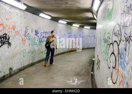 Un homme marche à travers un réseau piétonnier souterrain du métro, les murs couverts de graffitis. Banque D'Images