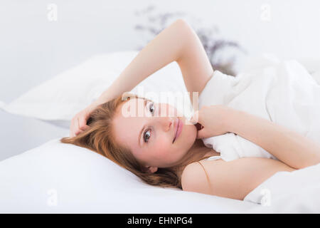 Woman laying in bed, tête sur l'oreiller, smiling at camera Banque D'Images