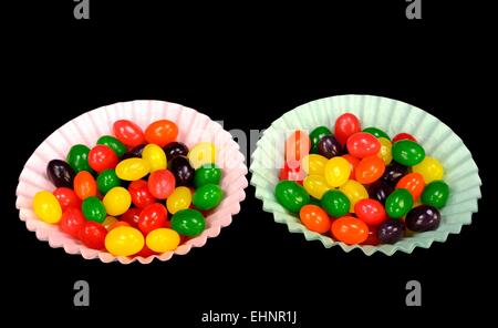 Fruit jelly beans dans beaucoup de couleurs dans les tasses de papier sur un fond noir. Banque D'Images