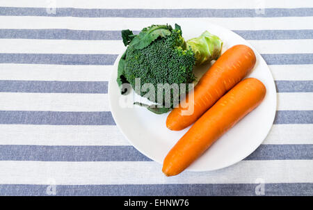 Le brocoli et deux carottes sur plaque blanche sur fond blanc à rayures Banque D'Images