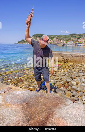 Un pêcheur traditionnel frappant un poulpe sur les rochers pour le grill à Limni town dans l'île d'Eubée, Grèce Banque D'Images