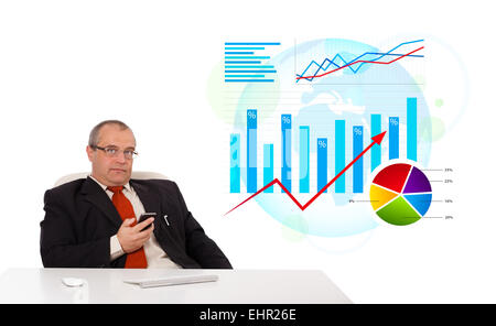 Businessman sitting at desk avec statistique et tenant une mobilephone Banque D'Images