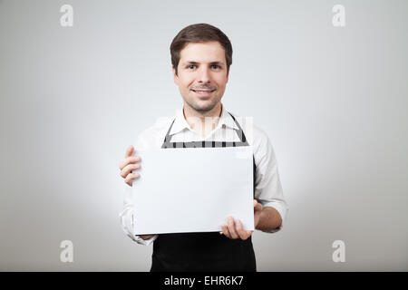 Homme avec un tablier et un tableau blanc sur fond gris Banque D'Images