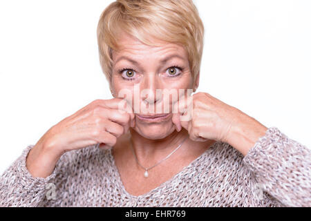 Belle femme d'âge moyen avec de courts cheveux blonds cherche à renverser les signes du vieillissement en tirant sur ses joues avec ses mains Banque D'Images