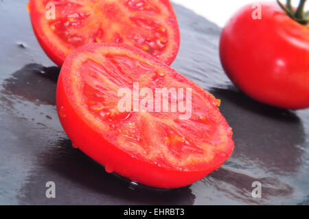 Libre de quelques tomates fraîches, l'un d'entre eux réduit de moitié, sur une surface en ardoise Banque D'Images