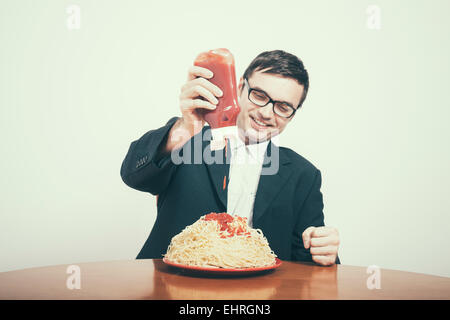 Le consumérisme heureux concept. Happy businessman pouring ketchup sur grand plat de pâtes. Banque D'Images