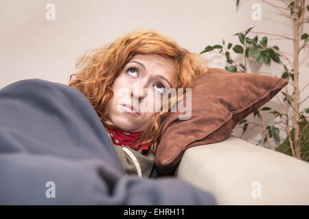 Sad lonely redhead woman looking up et de repos sur le canapé à la maison. Banque D'Images