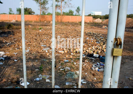 Un champ ouvert jonché d'ordures et les écorces de noix de coco est vu à travers une porte cadenassée à Skun, province de Kampong Cham, au Cambodge. Banque D'Images