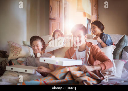 Groupe d'adolescents l'ouverture de boîtes à pizza on sofa in living room Banque D'Images